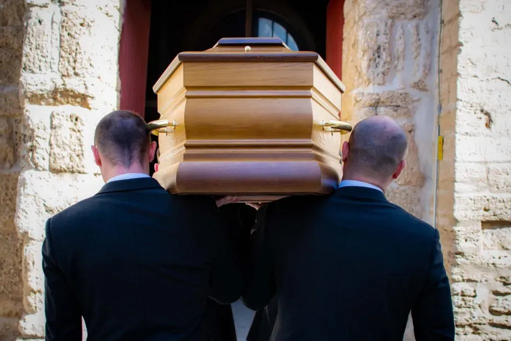 Porteurs funéraires en costume portant un cercueil en bois à l'entrée d'une église.